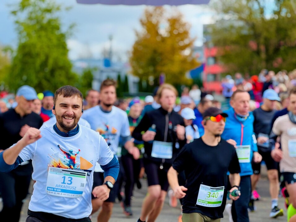 Uśmiechnięty mężczyzna z&nbsp;numerem 13 Arkadiusz biorący udział w&nbsp;biegu na&nbsp;15 km w&nbsp;otoczeniu innych biegaczy.