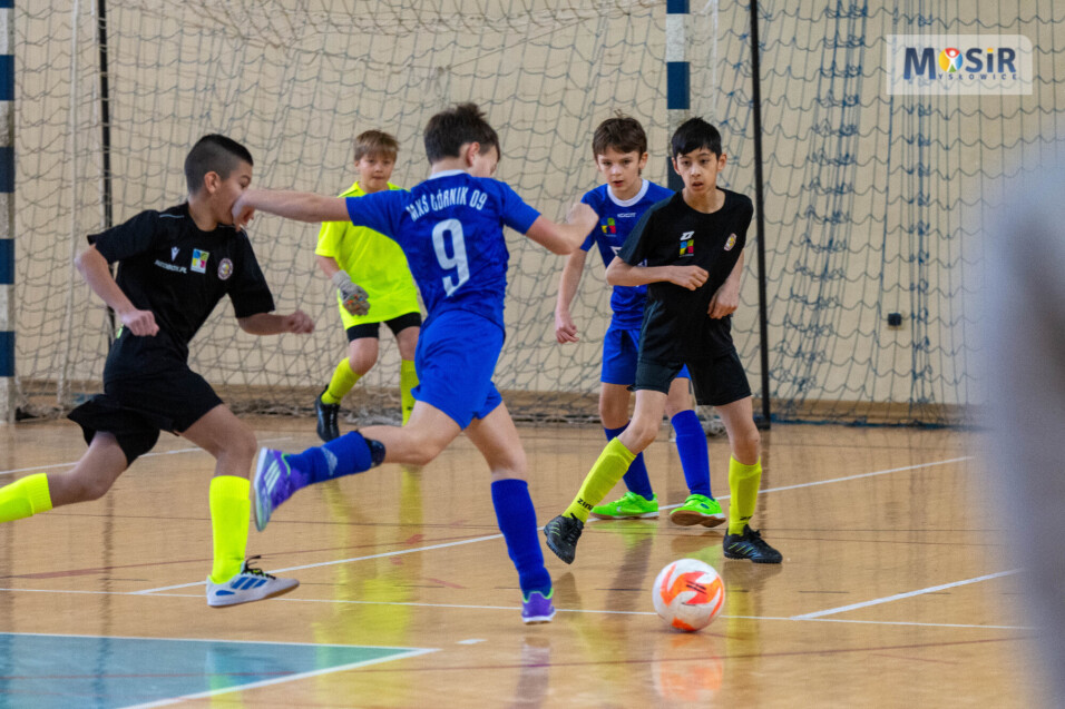 Próba strzelenia gola przez zawodnika w&nbsp;niebieskim stroju pod dużym pressingiem